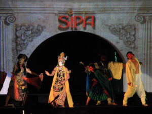 Para penari bertopeng dan berbusana tradisional tampil di atas panggung dengan latar belakang logo SIPA.