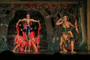 Penari wayang orang berbusana kesatria memegang busur panah berhadapan dengan tokoh putri dan raksasa di panggung teater.