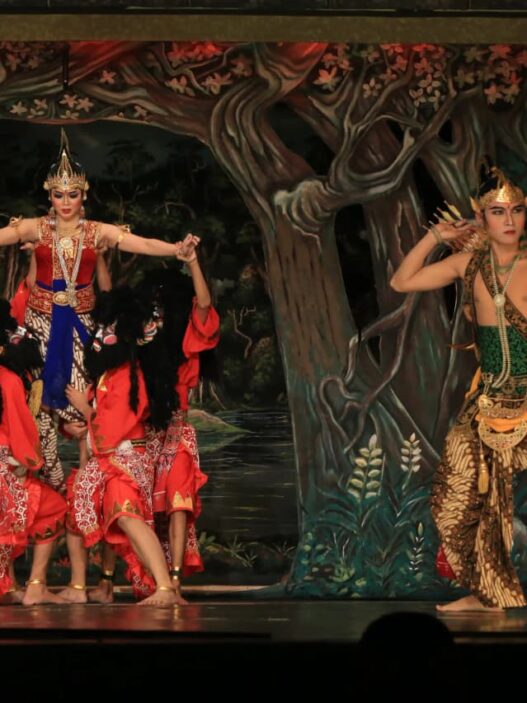 Penari wayang orang berbusana kesatria memegang busur panah berhadapan dengan tokoh putri dan raksasa di panggung teater.