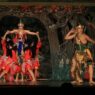 Penari wayang orang berbusana kesatria memegang busur panah berhadapan dengan tokoh putri dan raksasa di panggung teater.