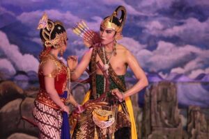 Dua pemeran wayang orang berbusana adat Jawa, Rama dan Sinta, berdiri berhadapan di atas panggung teater.
