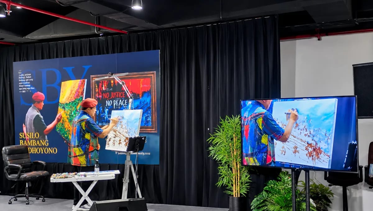 SBY mengenakan baret merah sedang melukis di kanvas saat sesi live painting.
