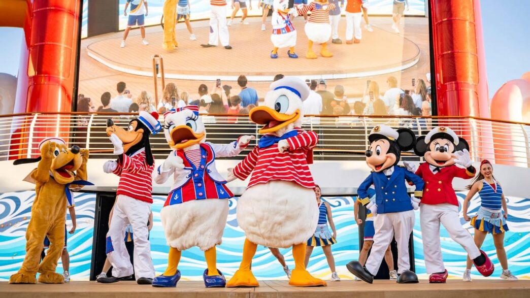 Karakter Disney dalam seragam pelaut meriah di panggung kapal pesiar Disney Cruise Line, berlatar belakang cerobong asap merah dan layar besar.