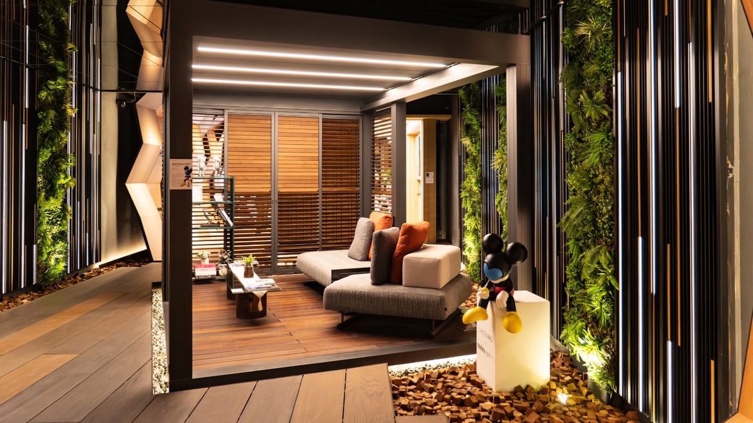 Instalasi paviliun kayu modern dengan sofa santai, pencahayaan LED hangat, dan dinding tanaman vertikal.