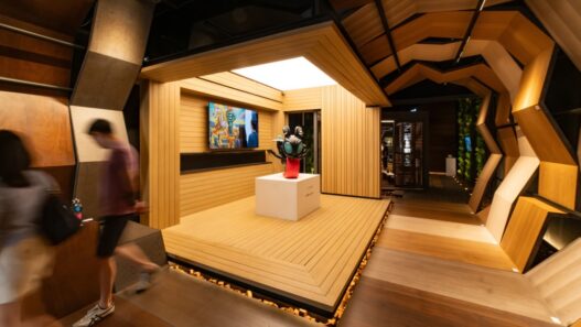 Booth pameran berstruktur kayu modern dengan patung seni di atas panggung kayu.