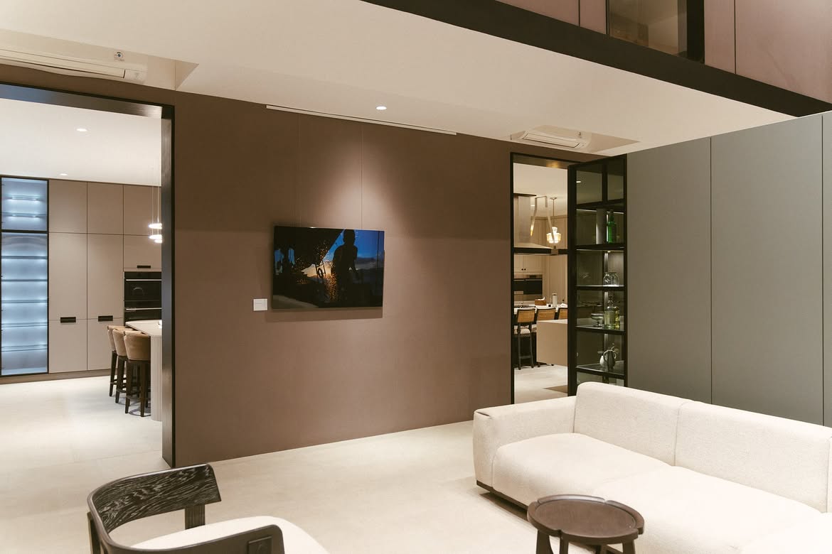Ruangan interior modern bernuansa abu-abu dan cokelat dengan sofa putih serta pencahayaan hangat.