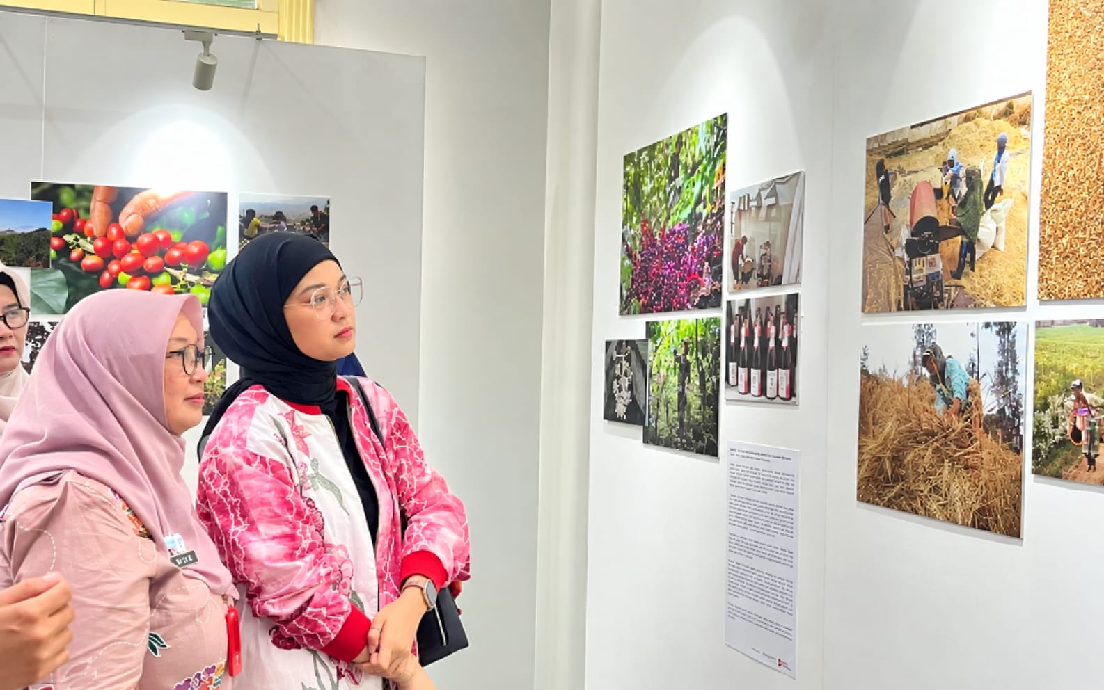Dua pengunjung perempuan berhijab sedang melihat deretan foto dokumenter pertanian dan pangan di dinding galeri.