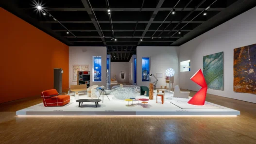 Pameran desain interior modern di galeri seni dengan instalasi furnitur artistik, pencahayaan hangat, dan lukisan dinding.