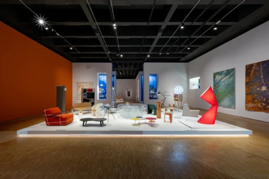 Pameran desain interior modern di galeri seni dengan instalasi furnitur artistik, pencahayaan hangat, dan lukisan dinding.