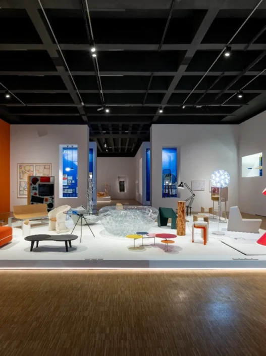 Pameran desain interior modern di galeri seni dengan instalasi furnitur artistik, pencahayaan hangat, dan lukisan dinding.