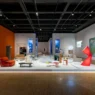 Pameran desain interior modern di galeri seni dengan instalasi furnitur artistik, pencahayaan hangat, dan lukisan dinding.