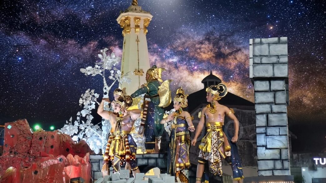 Para penari berbusana wayang tradisional tampil di atas kendaraan hias berlatar replika Tugu Jogja pada event karnaval malam.