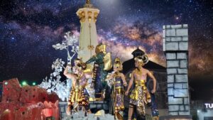 Para penari berbusana wayang tradisional tampil di atas kendaraan hias berlatar replika Tugu Jogja pada event karnaval malam.