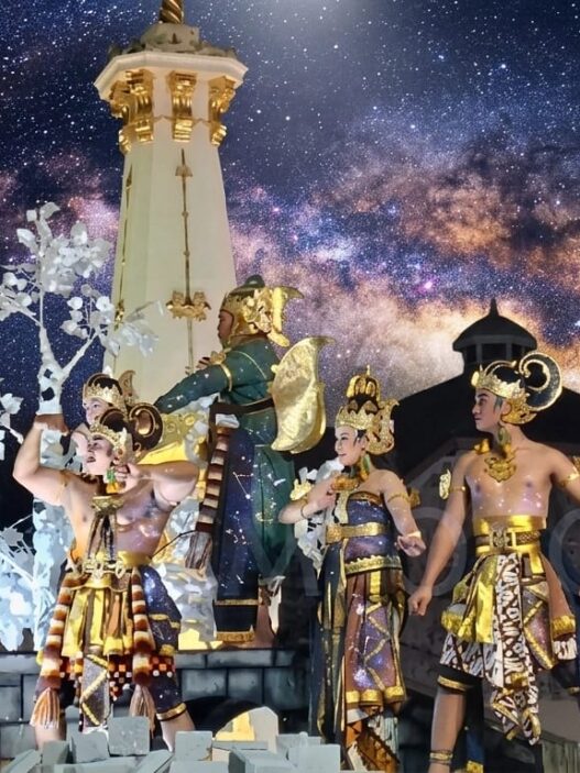 Para penari berbusana wayang tradisional tampil di atas kendaraan hias berlatar replika Tugu Jogja pada event karnaval malam.
