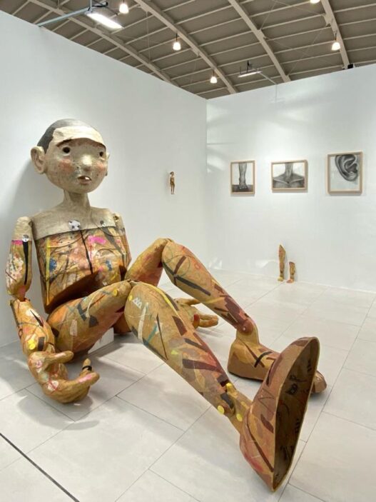 Instalasi patung figur manusia berukuran besar yang duduk di dinding galeri pameran seni kontemporer Art Jakarta 2026 di JIExpo Kemayoran.