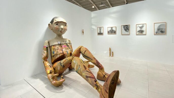 Instalasi patung figur manusia berukuran besar yang duduk di dinding galeri pameran seni kontemporer Art Jakarta 2026 di JIExpo Kemayoran.