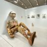 Instalasi patung figur manusia berukuran besar yang duduk di dinding galeri pameran seni kontemporer Art Jakarta 2026 di JIExpo Kemayoran.