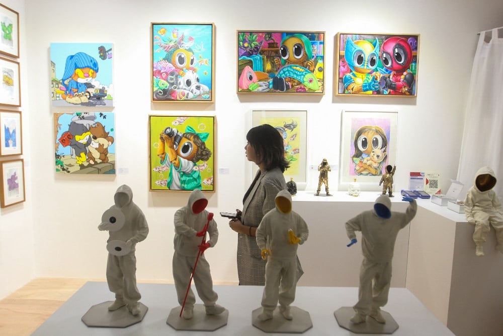 Pengunjung wanita sedang mengamati deretan lukisan pop art berwarna-warni dan patung figuratif putih di pameran seni kontemporer.