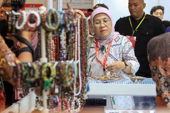 Seorang wanita berhijab pink sedang memilih perhiasan di stand pameran.
