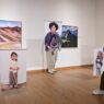 Seorang pengunjung wanita sedang memotret karya fotografi dokumenter yang dipamerkan di ruang galeri seni.