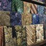 Berbagai lipatan kain batik dengan beragam motif dan warna tersusun rapi di rak kayu.