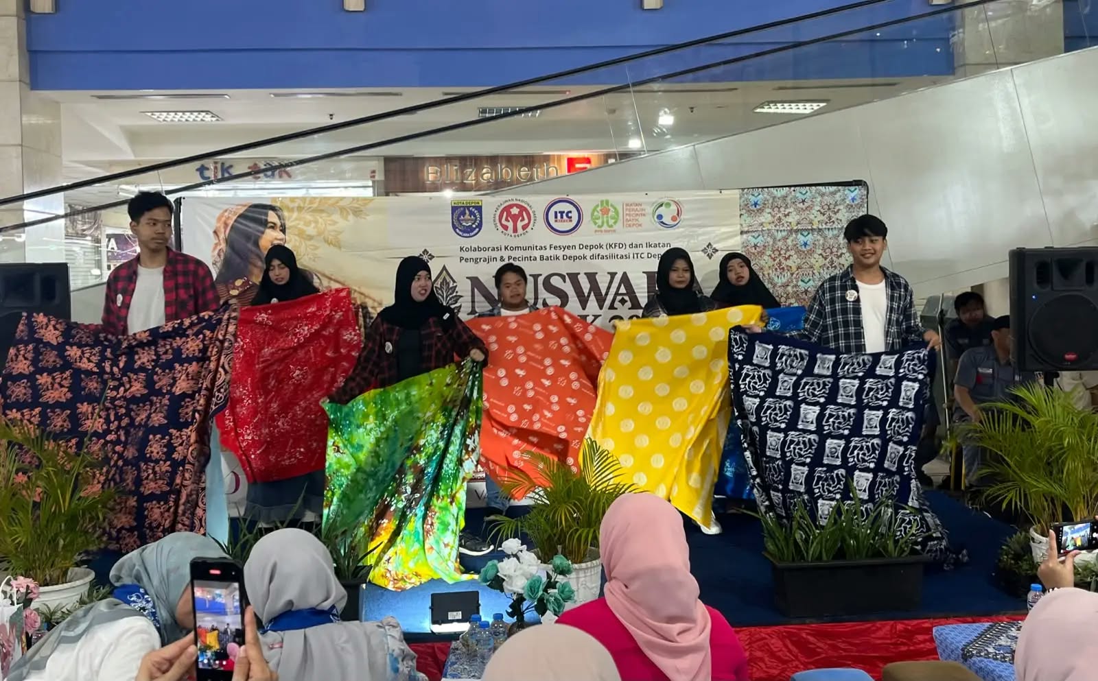 Sekelompok remaja membentangkan berbagai kain batik bermotif dan berwarna-warni di atas panggung pameran Nuswara Depok.