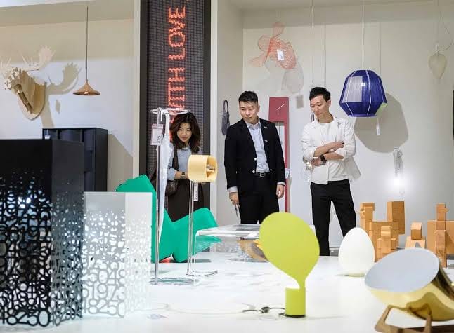 Tiga pengunjung melihat koleksi lampu unik dan furnitur artistik di pameran desain.