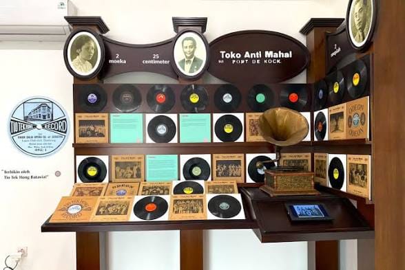 Display kayu klasik berhiaskan foto potret antik, deretan piringan hitam, sampul album vintage, serta sebuah pemutar gramofon berdaun corong kuningan.