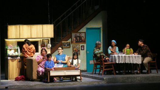 Para pemeran teater dalam set panggung berupa interior rumah modern dan area makan keluarga.