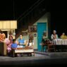Para pemeran teater dalam set panggung berupa interior rumah modern dan area makan keluarga.