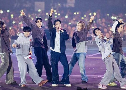 Enam anggota grup K-Pop ENHYPEN tampil energik di atas panggung konser besar dengan latar belakang penonton yang memegang lightstick menyala.