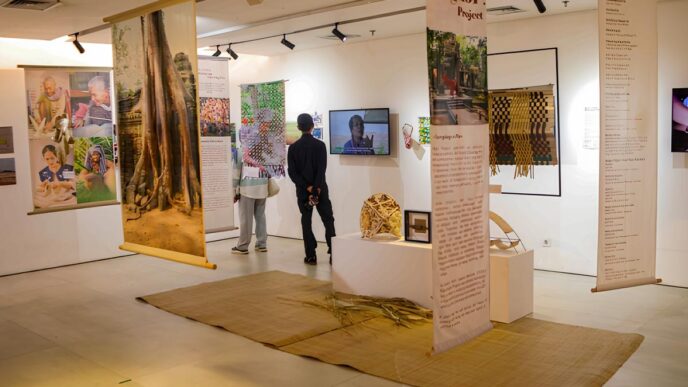 Pengunjung sedang melihat pameran seni bertema Angkor Project dengan spanduk gantung, instalasi kerajinan, dan layar video.