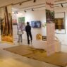 Pengunjung sedang melihat pameran seni bertema Angkor Project dengan spanduk gantung, instalasi kerajinan, dan layar video.