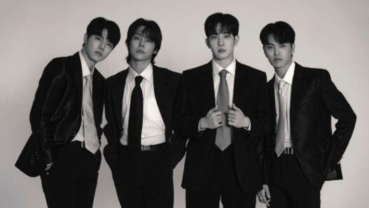 Foto hitam-putih empat anggota band DAY6 (Young K, Sungjin, Wonpil, dan Dowoon) berpose formal mengenakan setelan jas dan dasi rapi dengan latar belakang putih polos.