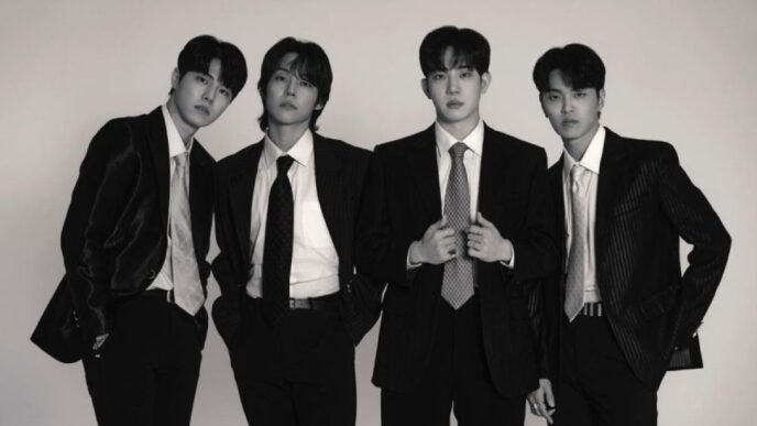 Foto hitam-putih empat anggota band DAY6 (Young K, Sungjin, Wonpil, dan Dowoon) berpose formal mengenakan setelan jas dan dasi rapi dengan latar belakang putih polos.