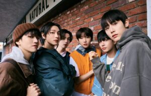 Enam anggota boyband K-pop BOYNEXTDOOR berpose gaya casual streetwear di luar ruangan dengan latar belakang dinding bata merah.