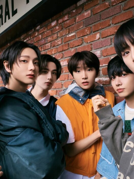 Enam anggota boyband K-pop BOYNEXTDOOR berpose gaya casual streetwear di luar ruangan dengan latar belakang dinding bata merah.