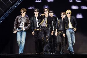 Enam anggota boyband K-pop BOYNEXTDOOR tampil di atas panggung mengenakan kacamata hitam, jaket gaya rock/edgy, dan celana jeans.