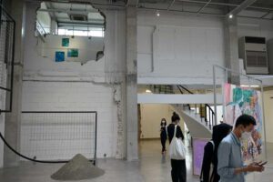 Suasana ruang galeri seni ROH Jakarta yang bergaya industrial modern, memperlihatkan pengunjung sedang melihat karya lukisan, gundukan pasir di lantai, serta dinding beton berlubang.