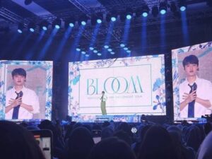 Suasana megah konser Doh Kyung Soo 'BLOOM' dilihat dari area penonton. Panggung dihiasi tiga layar LED besar yang menayangkan tulisan 'BLOOM DOH KYUNG SOO ASIA FAN CONCERT TOUR' serta penampilannya secara langsung dengan sorotan lampu panggung biru.