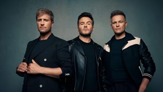 Tiga anggota grup musik Westlife (Kian Egan, Shane Filan, dan Nicky Byrne) berdiri bersama dalam pakaian hitam berpose untuk foto studio.