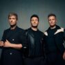 Tiga anggota grup musik Westlife (Kian Egan, Shane Filan, dan Nicky Byrne) berdiri bersama dalam pakaian hitam berpose untuk foto studio.