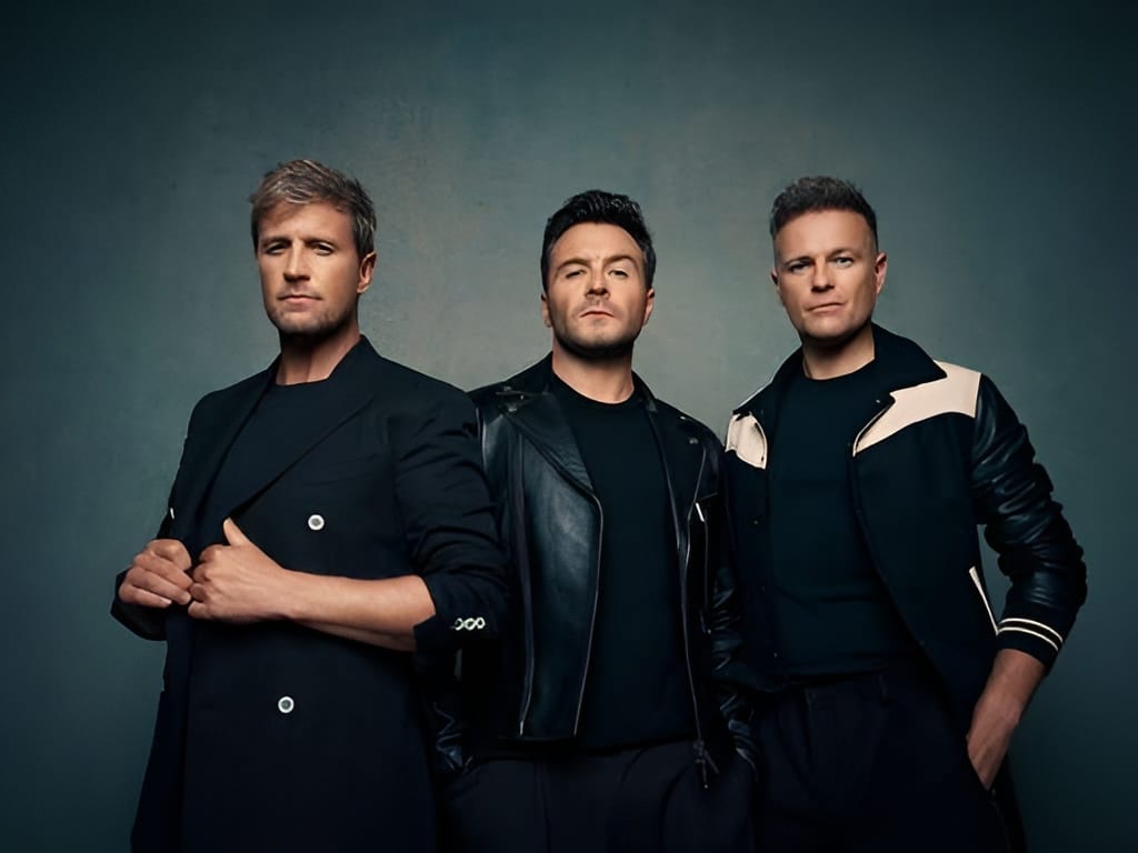Tiga anggota grup musik Westlife (Kian Egan, Shane Filan, dan Nicky Byrne) berdiri bersama dalam pakaian hitam berpose untuk foto studio.