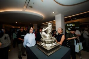 Pengunjung mengamati sebuah patung logam berwarna perak berbentuk figur di atas alas dalam pameran seni.