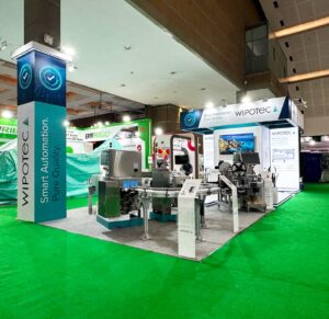 "Stan pameran WIPOTEC dengan branding 'Smart Automation. Pure Quality' menampilkan mesin otomatisasi industri dan sistem konveyor di dalam aula pameran."