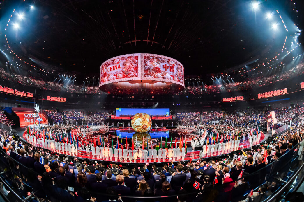 Suasana megah stadium dalam panggung pembukaan WorldSkills Shanghai 2026 yang dipenuhi bendera peserta dan layar silinder besar bertuliskan China.